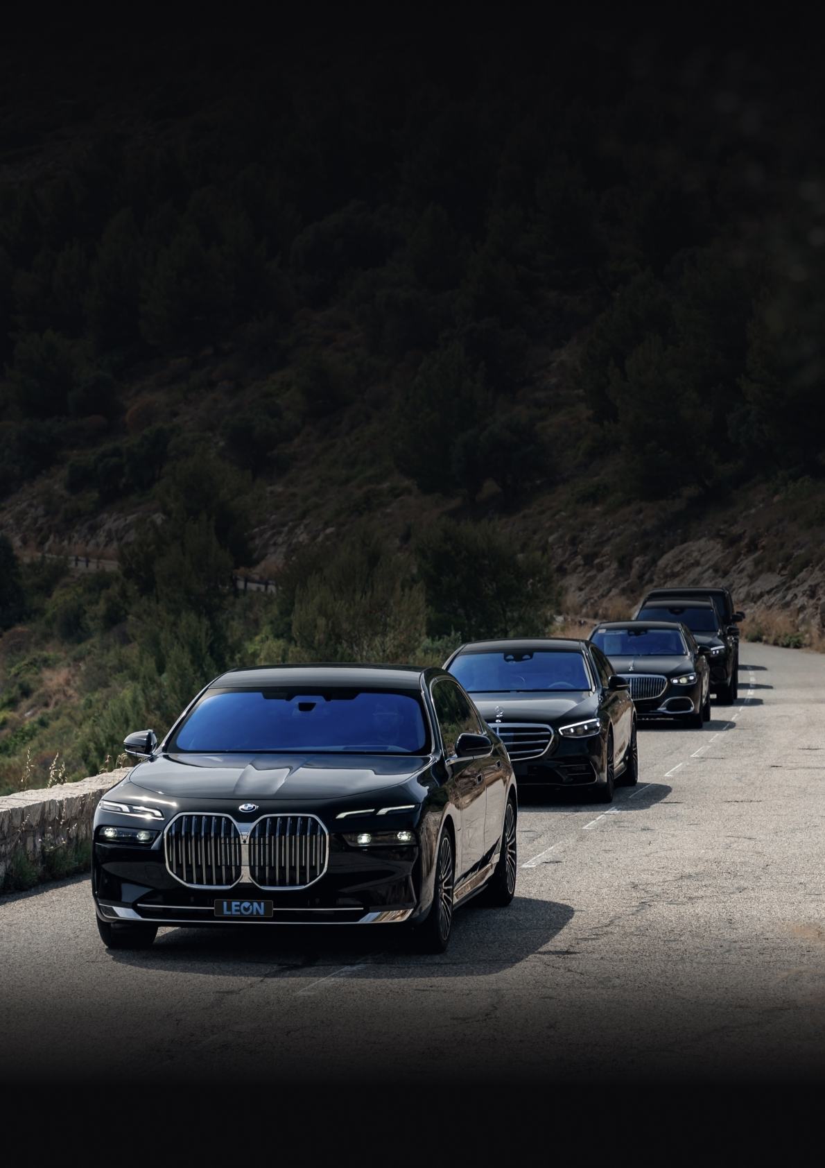 A convoy of four black LEON saloons on a coastal mountain road
